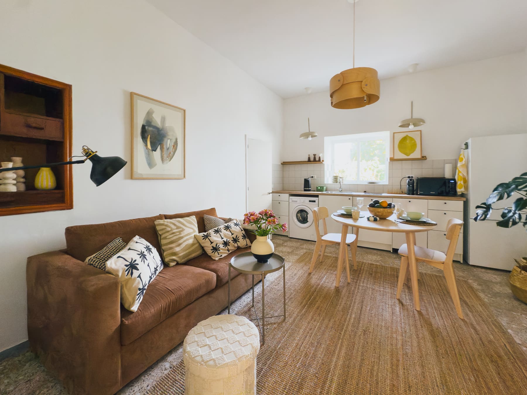 Salón luminoso con sofá de cuero marrón, mesa de comedor redonda y la cocina al fondo
